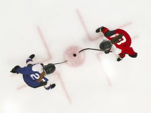 Two women brace for a faceoff in the middle of an ice hockey rink.