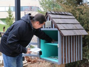 A man wearing a black jacket places children's books in a wooden little library.