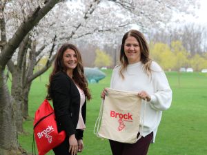 Fourth-year Psychology student and Research Assistant Cassandra Campanella and Brock Health Management and Wellness Manager Martina Ciglenecki hold up promotional bags while standing among the campus cherry blossom trees to promote the 21st Annual Employee Wellness Day, returning Tuesday June 20.