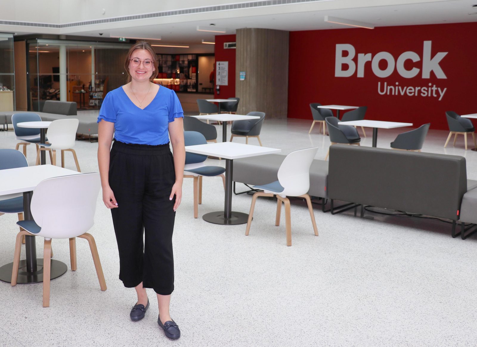 A woman stands in an indoor atrium in front of a painted wall that says ‘Brock’.