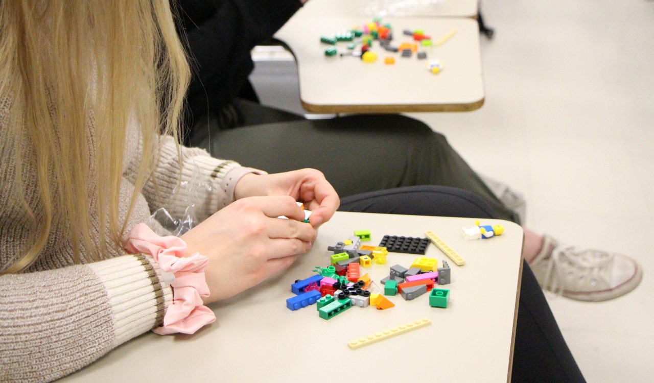Hands play with multicoloured toy building blocks on a desk in a classroom.
