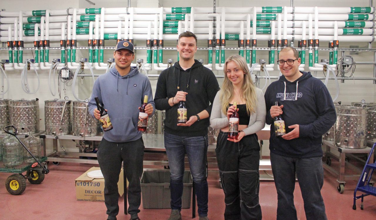Four students holding wine bottles in a teaching winery lab.
