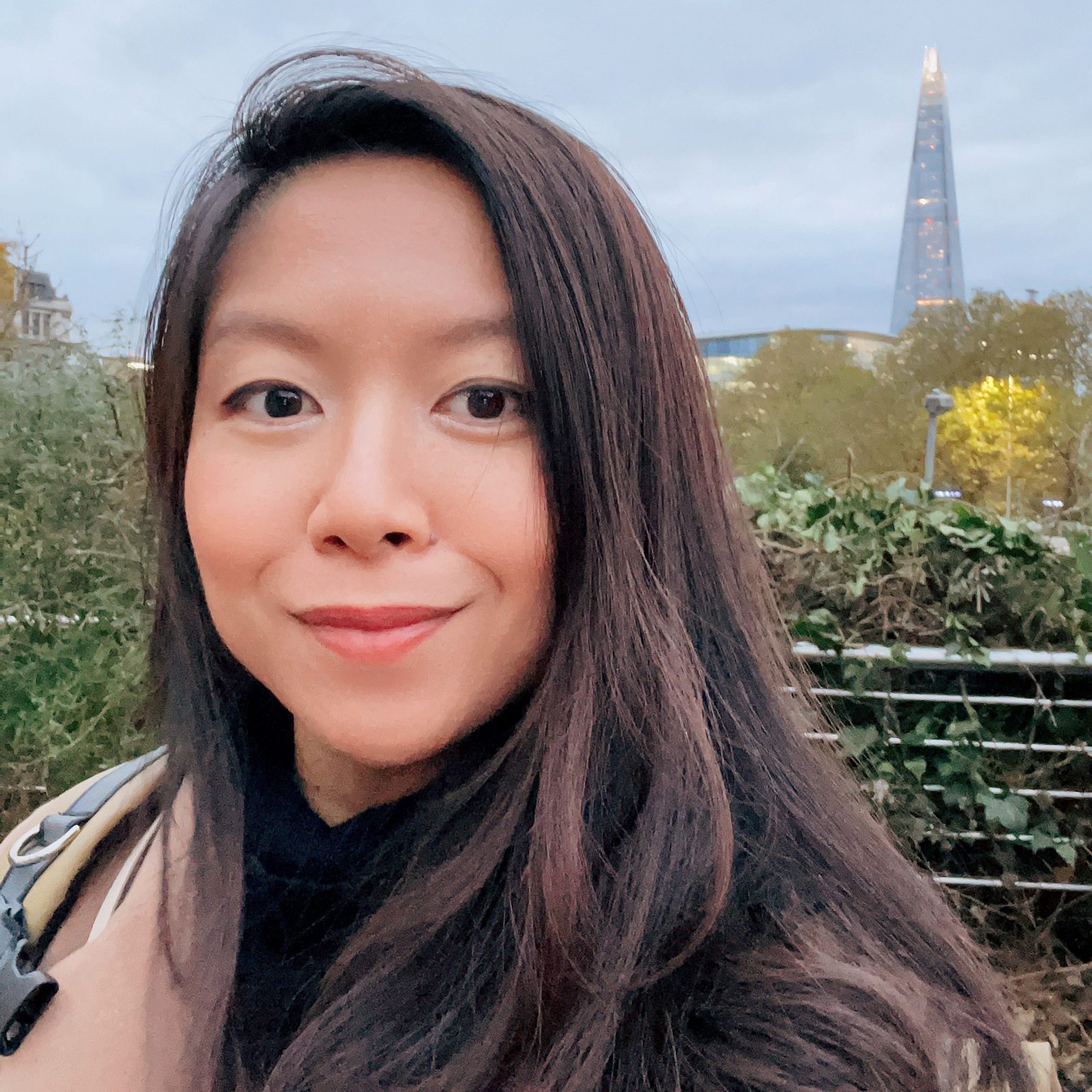 Close-up portrait of Rachel Song taken outside with a city in the distance. She is wearing a light brown jacket and black shirt.