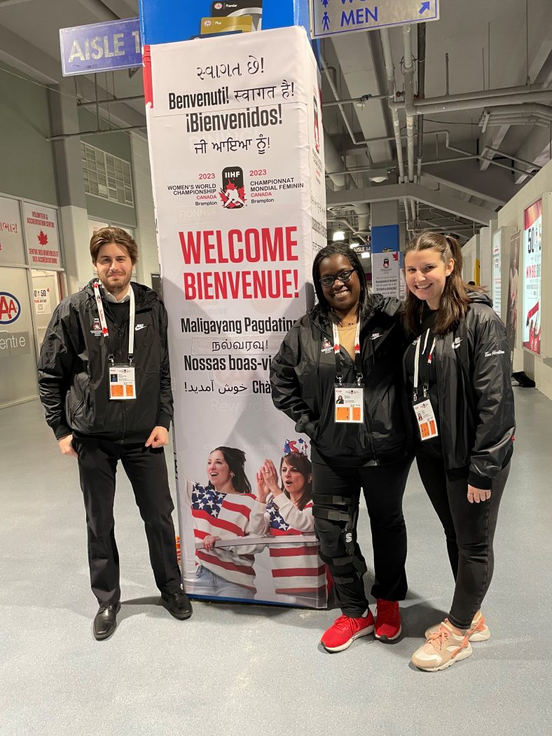 Three people stand beside a pull-up banner at the 2023 Women's World Hockey Championship.