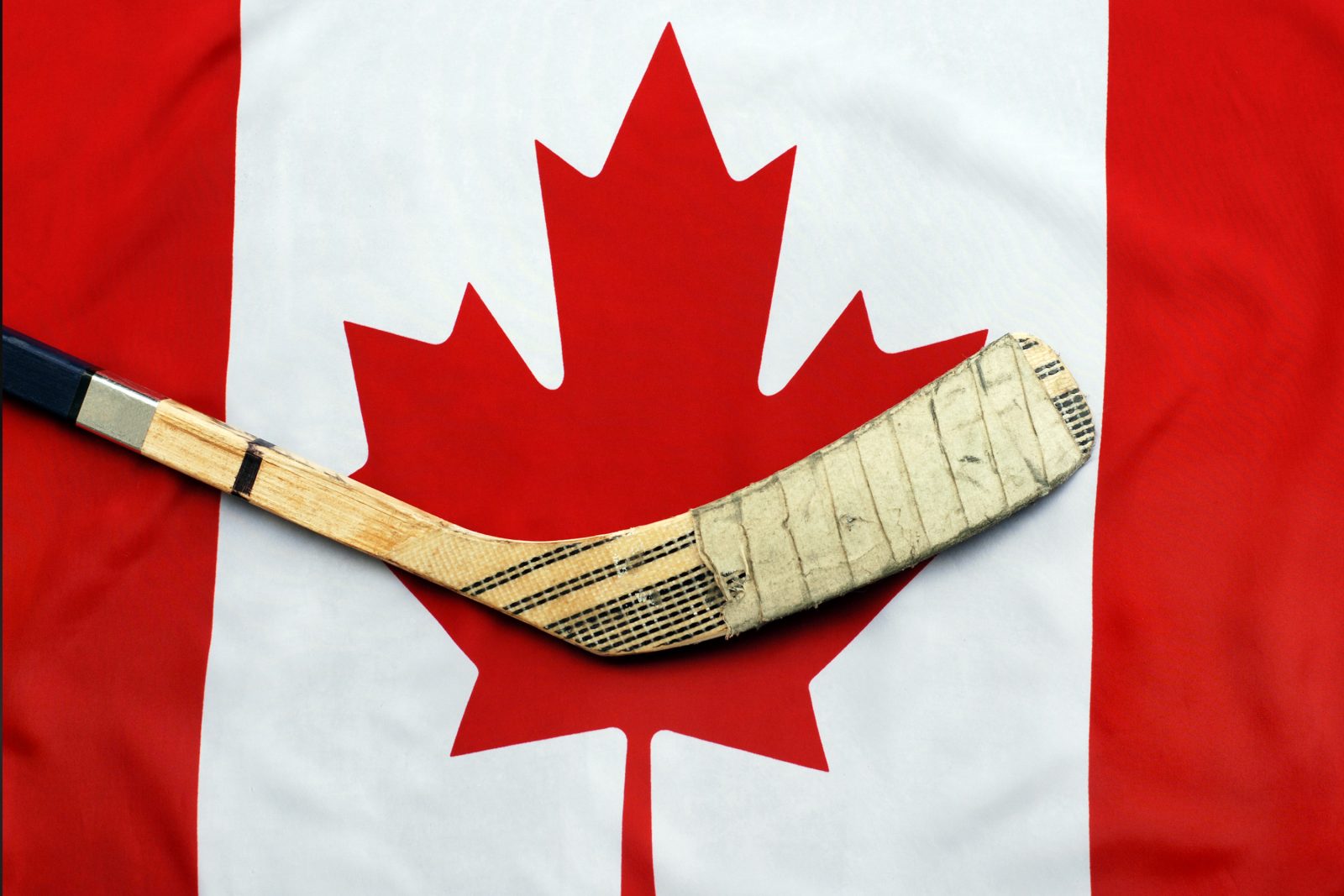 A hockey stick lays across a Canadian flag.