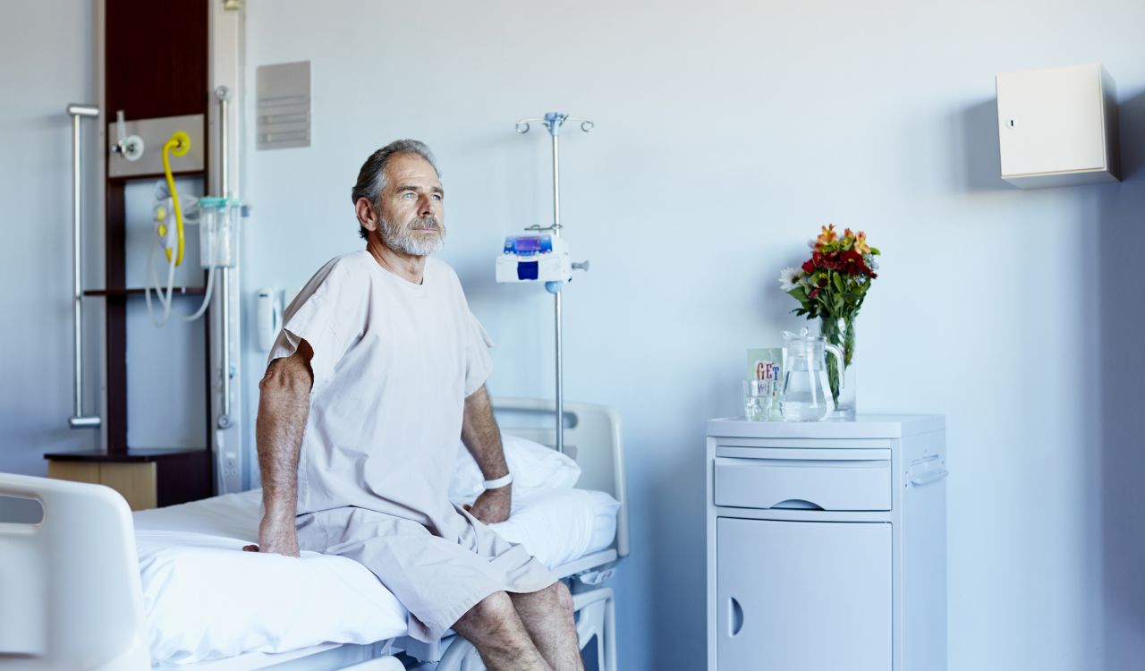 Thoughtful mature man looking away while sitting on a bed in a hospital ward.