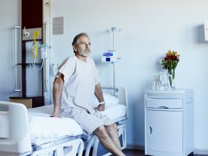 Thoughtful mature man looking away while sitting on a bed in a hospital ward.
