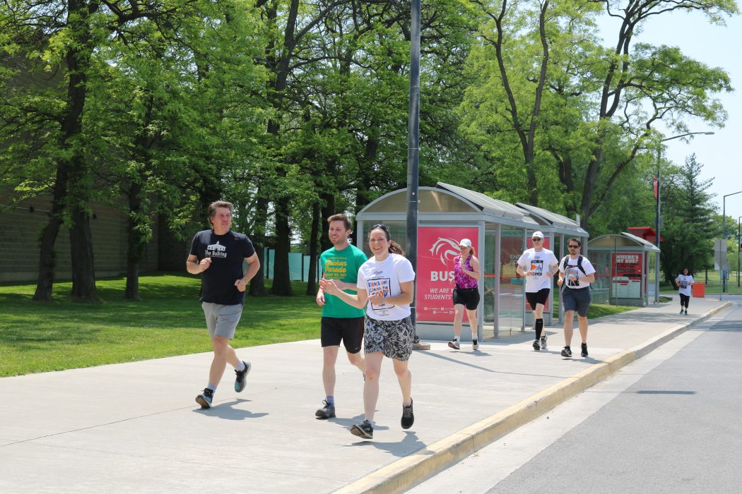 A group of runners run along an outdoor sidewalk at Brock University.