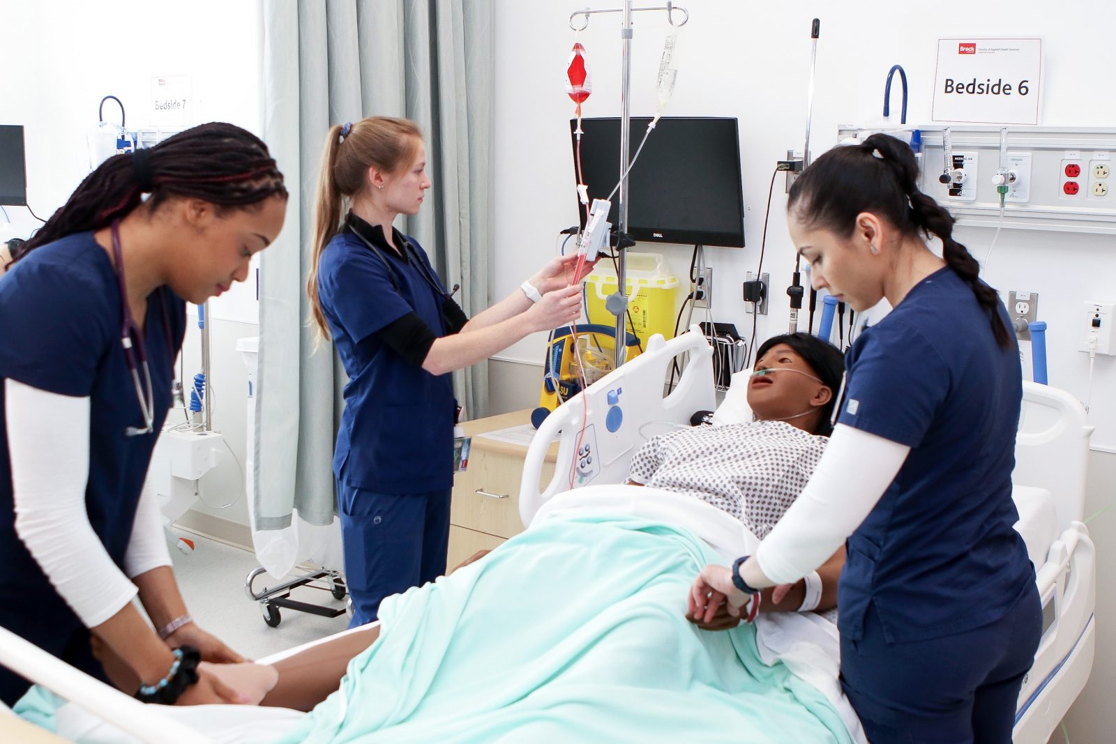 Three nursing students check the blood levels and pulse of a patient simulator.