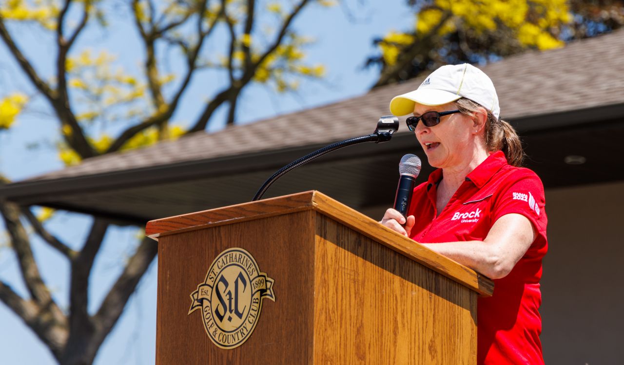 rock University’s President and Vice-Chancellor Lesley Rigg speaks at a podium outside at a golf course.