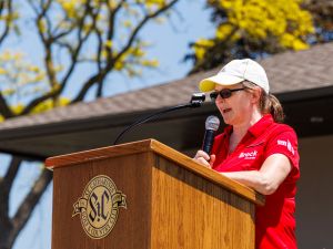 rock University’s President and Vice-Chancellor Lesley Rigg speaks at a podium outside at a golf course.