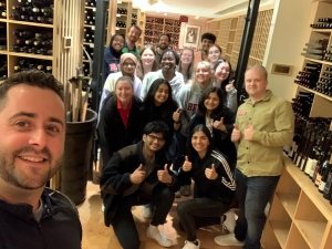 A group of people take a selfie in a wine cellar.