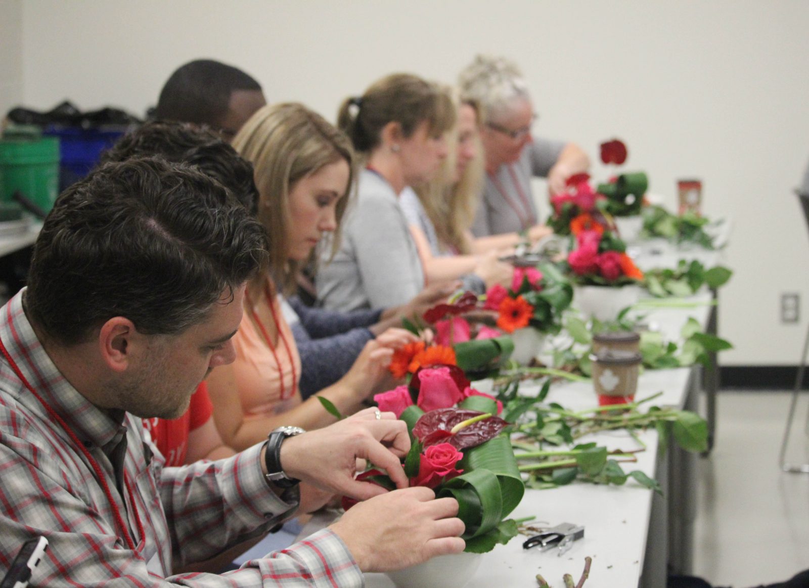 Seven people sit at a table arranging flowers.