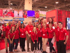 A group of 18 people pose as a group in a conference venue decorated with Brock branding and messaging.