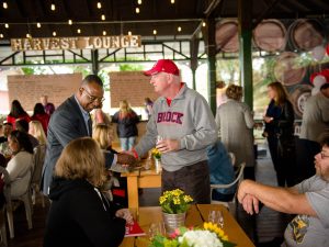 A group of Brock alumni and employees attend a celebration in an outdoor pavilion. A lighted sign in the background says “Harvest Lounge.”