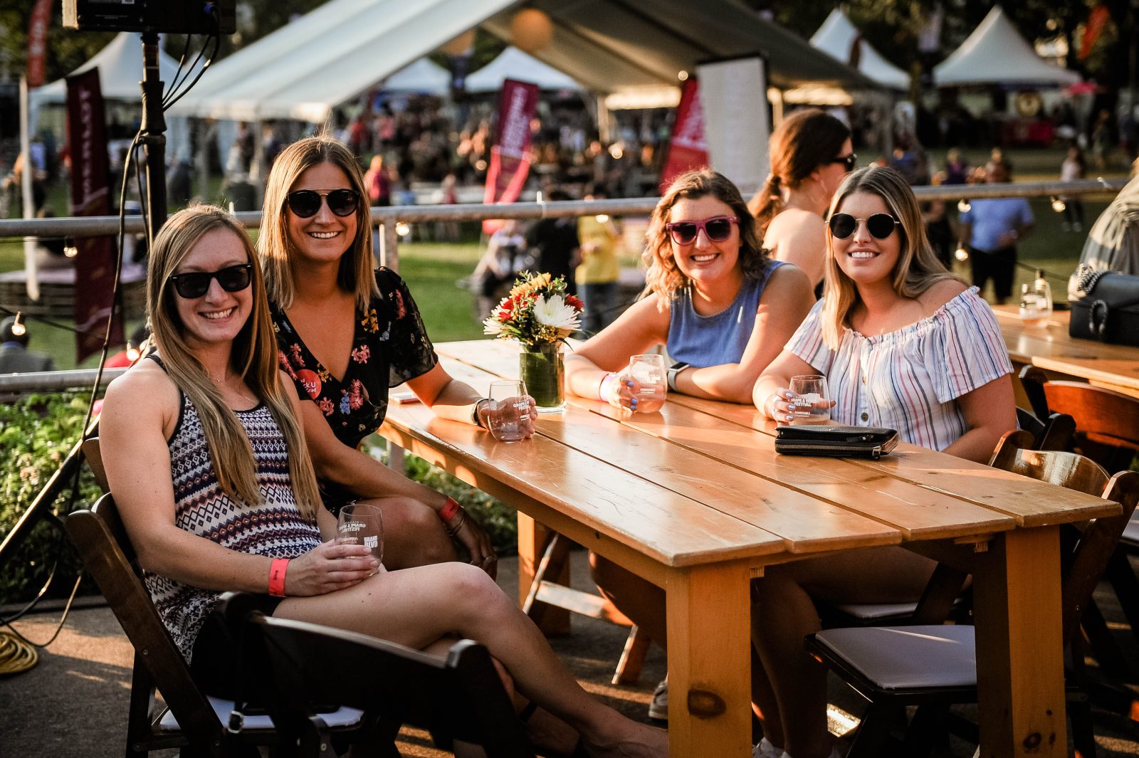 Four women sit at a picnic table at an outdoor wine festival.