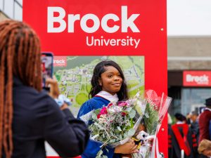 A new graduate poses with bouquets of flowers at Brock University's Convocation ceremony.