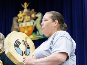 An Indigenous woman drums at a graduation ceremony.