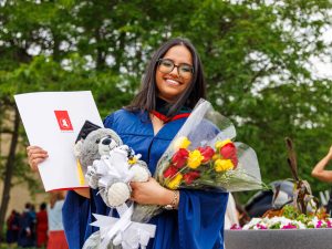 A Brock graduate poses outside with her diploma while holding a bouquet of flowers.