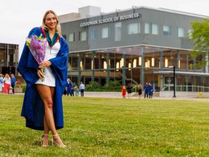 A smiling Brock graduate poses with flowers outside the Goodman School of Business building after Convocation.
