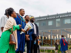 A new Brock graduate in a Convocation gown poses with loved ones outside the Goodman School of Business building.