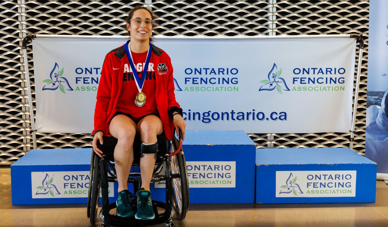 A woman sits in a wheelchair wearing sports gold and silver medals.
