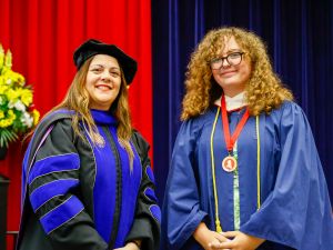 A woman in academic regalia stands beside young woman wearing a graduation gown and a medal.