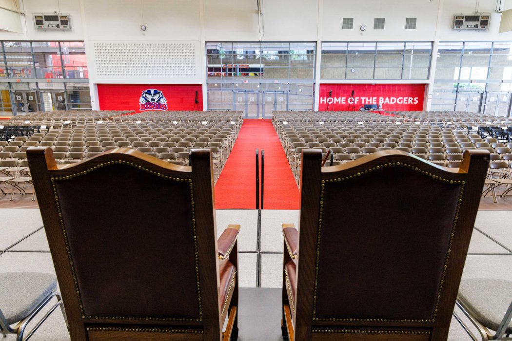 Ceremonial chairs on a stage face a large auditorium full of additional chairs.