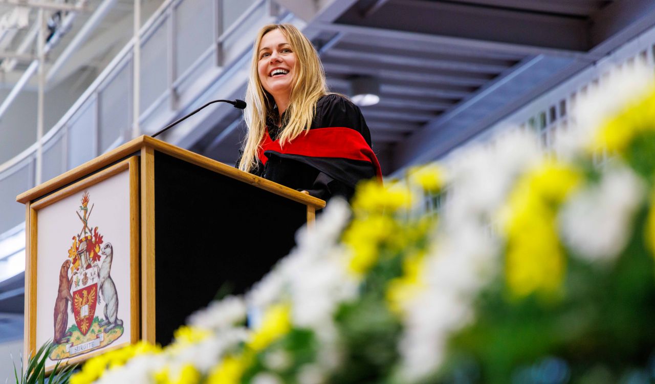Erin Panda stands behind a podium speaking to graduates during a Brock University Convocation ceremony.