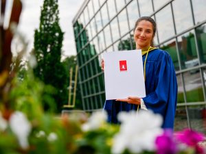 A young woman in a graduation gown holds up her diploma outside Brock's Convocation ceremony.