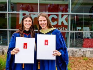 Two Brock graduates pose for photos with their diplomas.