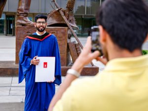 A new graduate in a gown gets his photo taken outside by a loved one after Convocation.