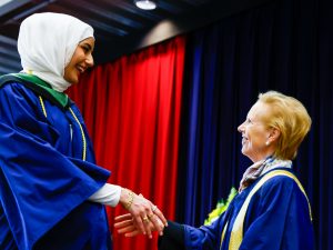 Two women in academic robes shake hands on stage during Brock's Convocation ceremony.