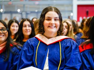 A graduating Brock University student smiles for a photo while sitting in a Convocation.