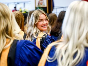 A graduating Brock University student smiles over her shoulder while sitting in a Convocation.