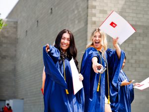 Two women in graduation gowns cheer outside Brock University's Convocation ceremony.
