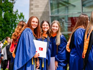 Three smiling Brock University graduates stand side-by-side outside after their Convocation ceremony.