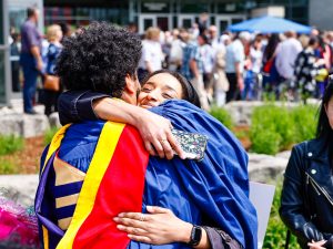 A new Brock University graduate hugs a loved one outside after his Convocation ceremony.