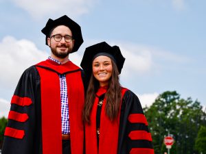 A man and a woman in academic robes pose outside at Brock University after Convocation.