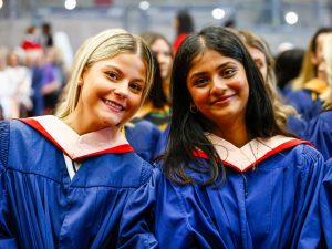 Two graduating students smile for a photo while sitting in a Convocation ceremony.