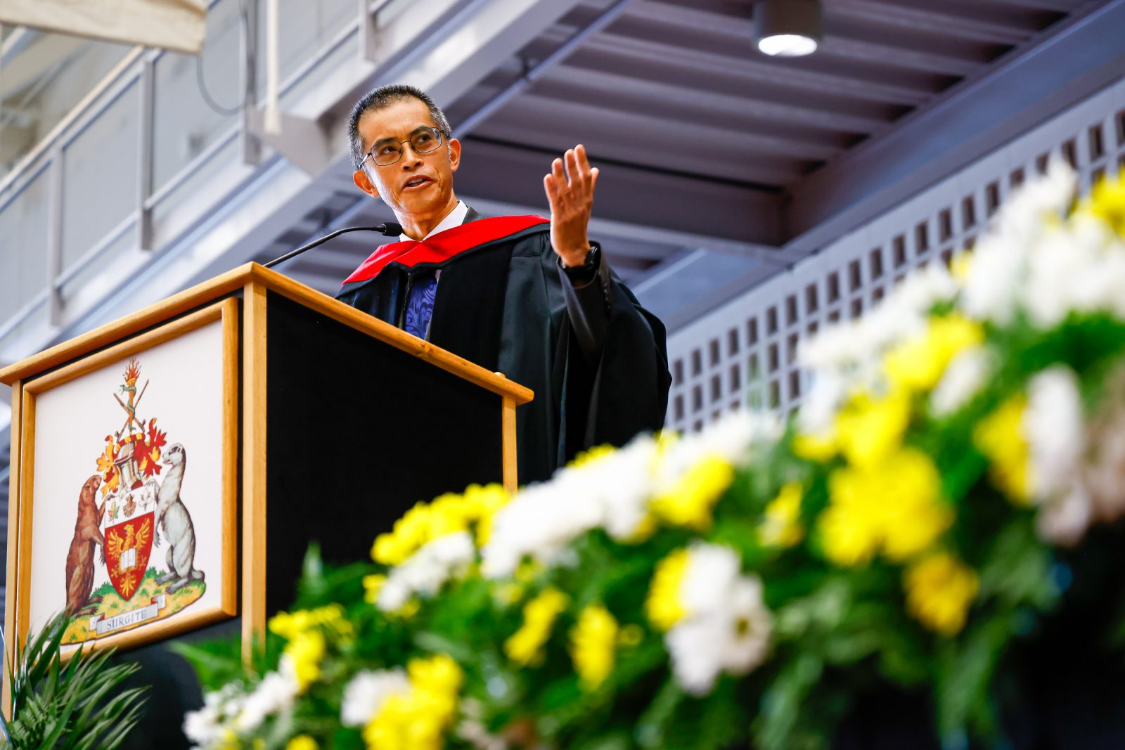 Stephen Cheung, dressed in academic regalia, speaking at a podium on a stage during a Brock University Convocation ceremony.