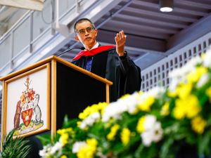 Stephen Cheung, dressed in academic regalia, speaking at a podium on a stage during a Brock University Convocation ceremony.