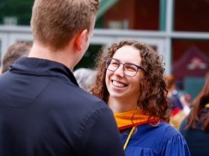 A woman in a convocation robe smiles while speaking to a man who is facing away from the camera.