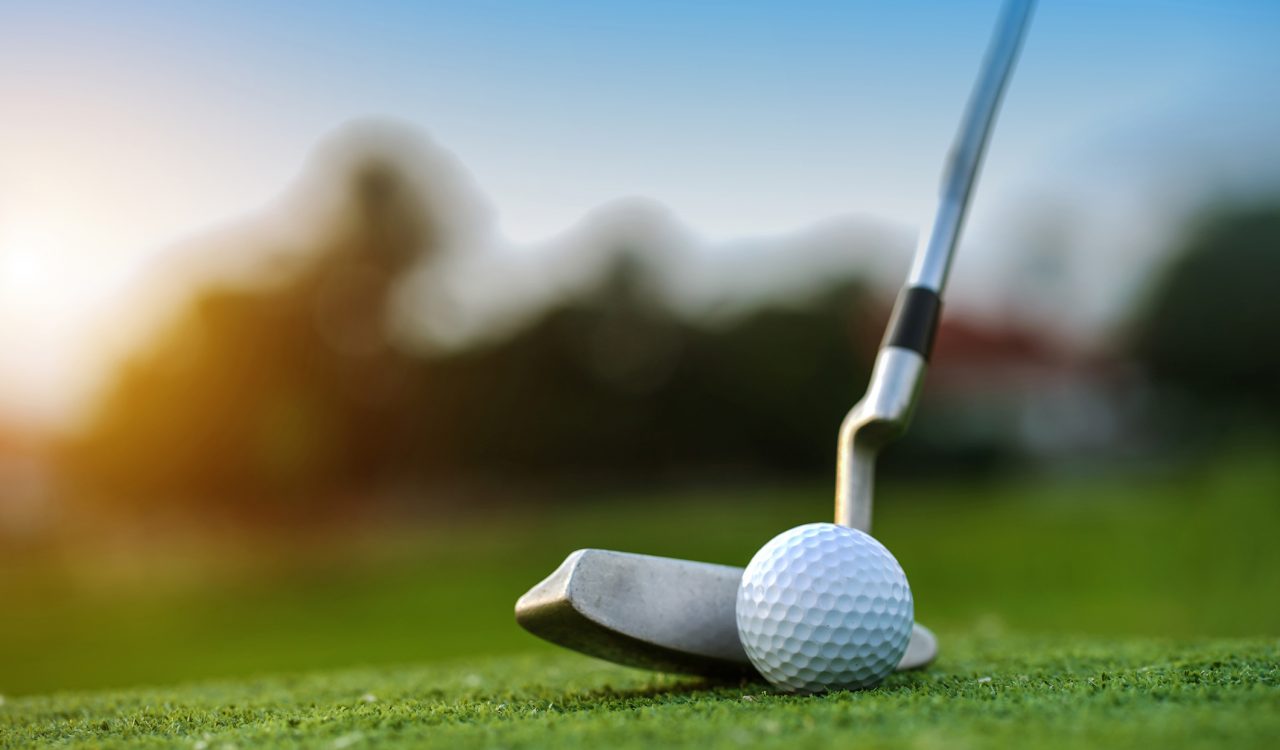 A golf club connecting with a golf ball on a green lawn.