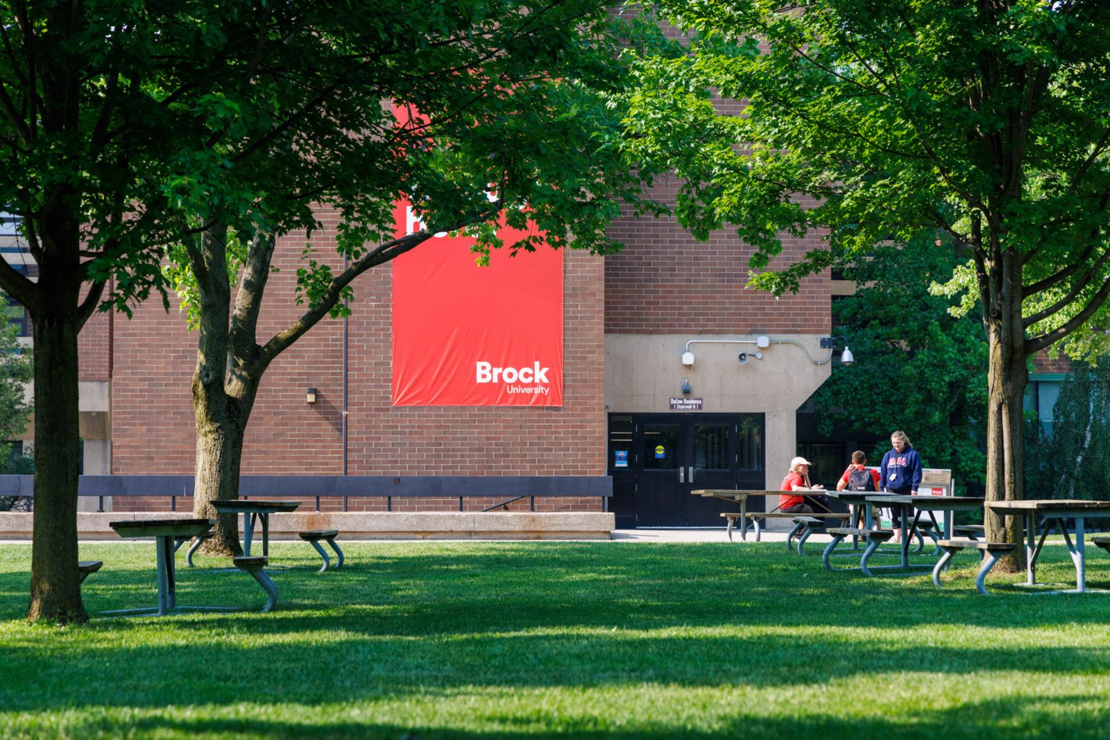 Three people sit at a picnic table under a tree in Brock's Jubilee Court.