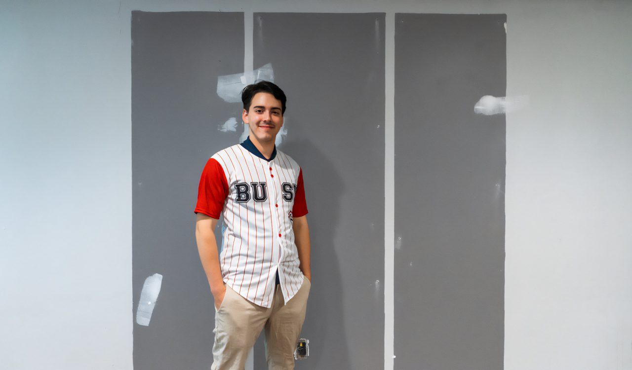 A man stands in front of a blank wall.