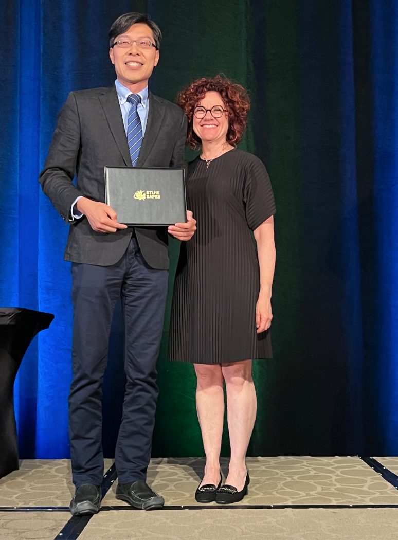 A man stands holding an award stands beside a woman on stage during an awards ceremony.