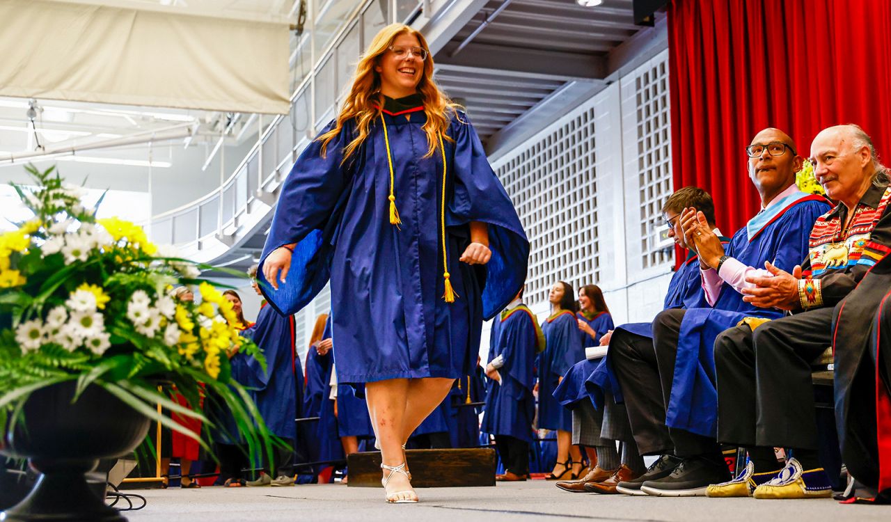 A woman in a graduation gown walks across the stage during a Convocation ceremony.