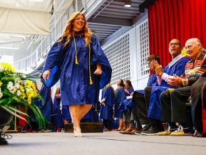 A woman in a graduation gown walks across the stage during a Convocation ceremony.