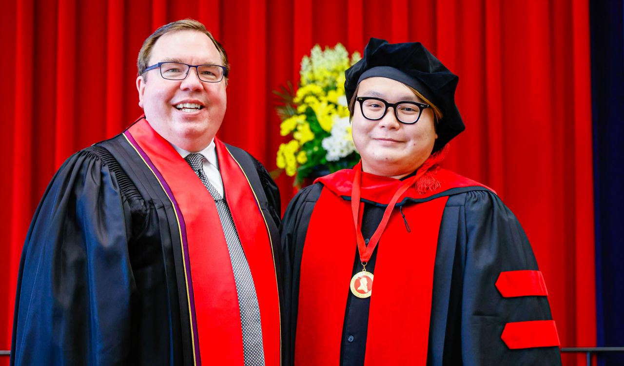Two men in academic regalia stand on stage during Convocation.